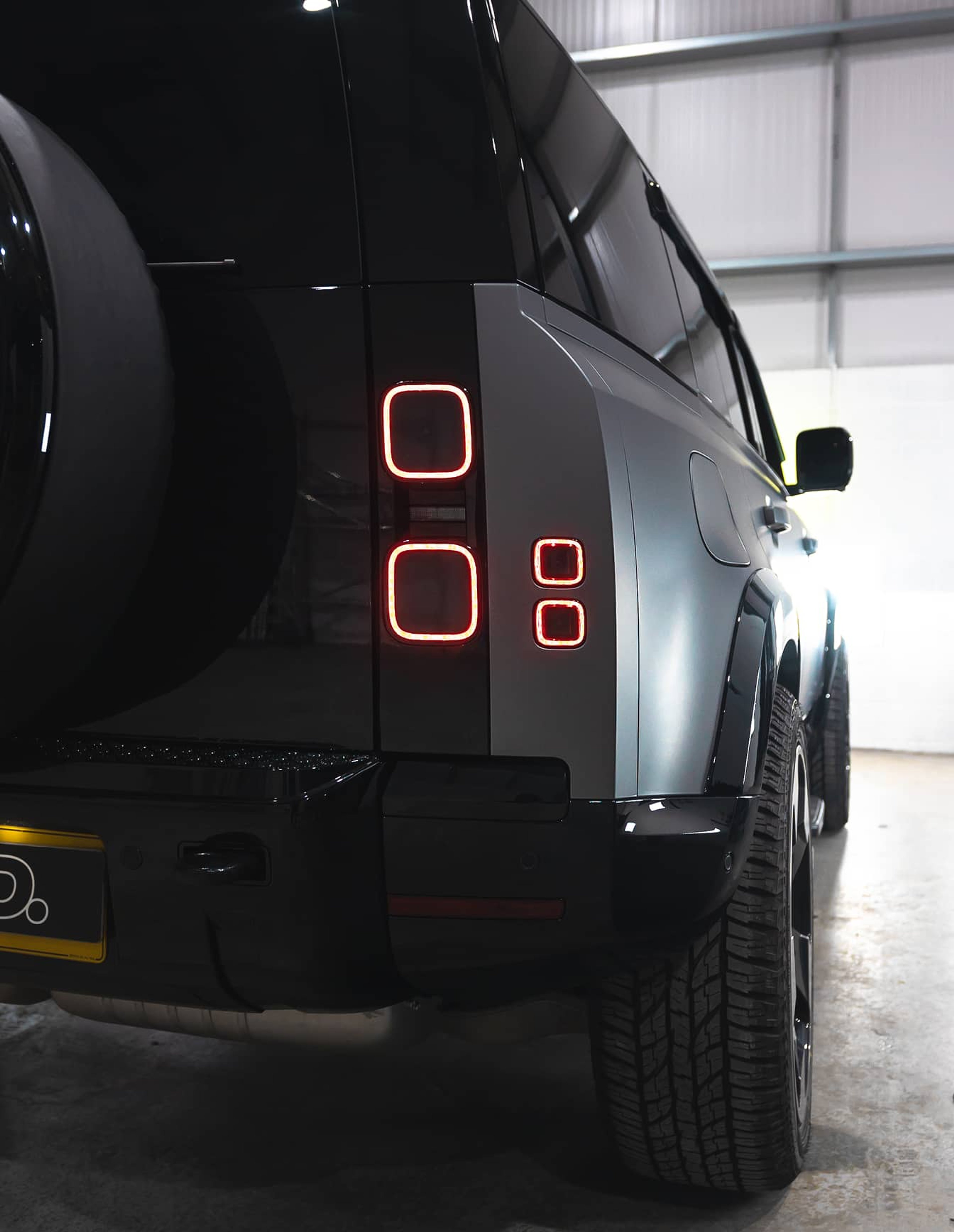 A custom Forge Land Rover Defender 110 with glowing red taillights is parked indoors on a concrete floor.