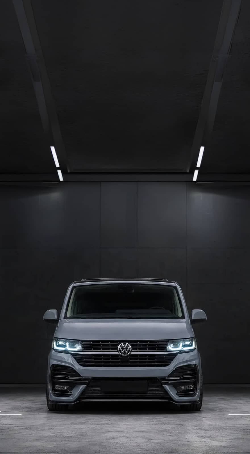 A custom Forge Volkswagen T6.1, painted gray, is parked head-on in a dark, minimalist garage with bright overhead strip lighting.