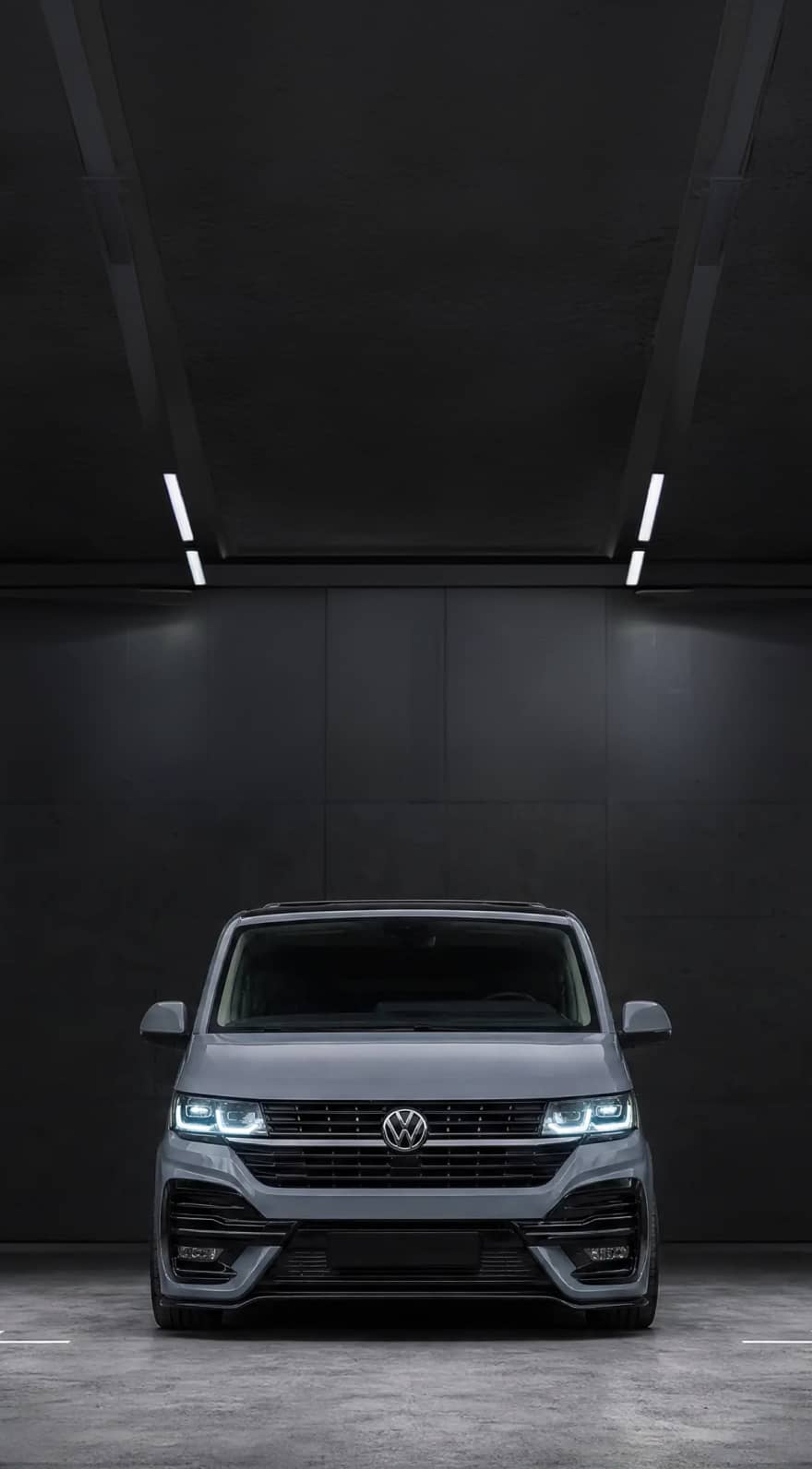 A custom Forge Volkswagen T6.1, painted gray, is parked head-on in a dark, minimalist garage with bright overhead strip lighting.