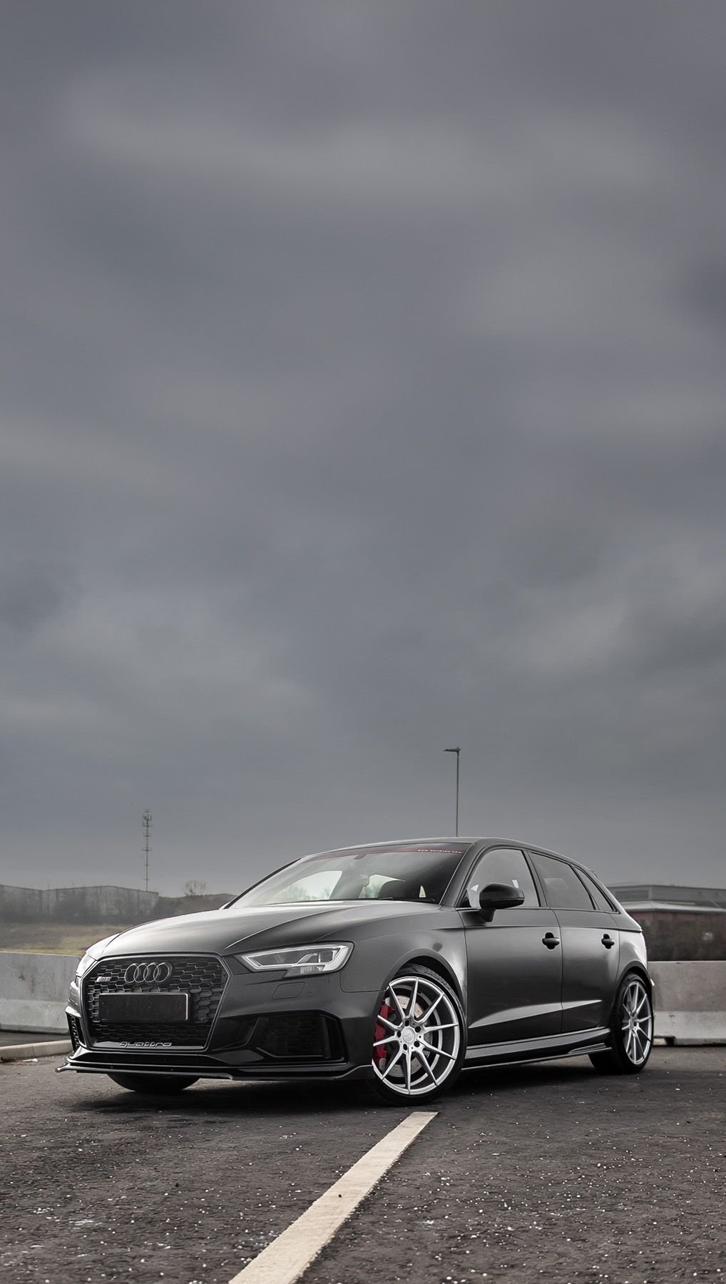 A matte black custom Forge Audi RS3 with silver wheels sits parked on an asphalt lot under an overcast, moody sky.