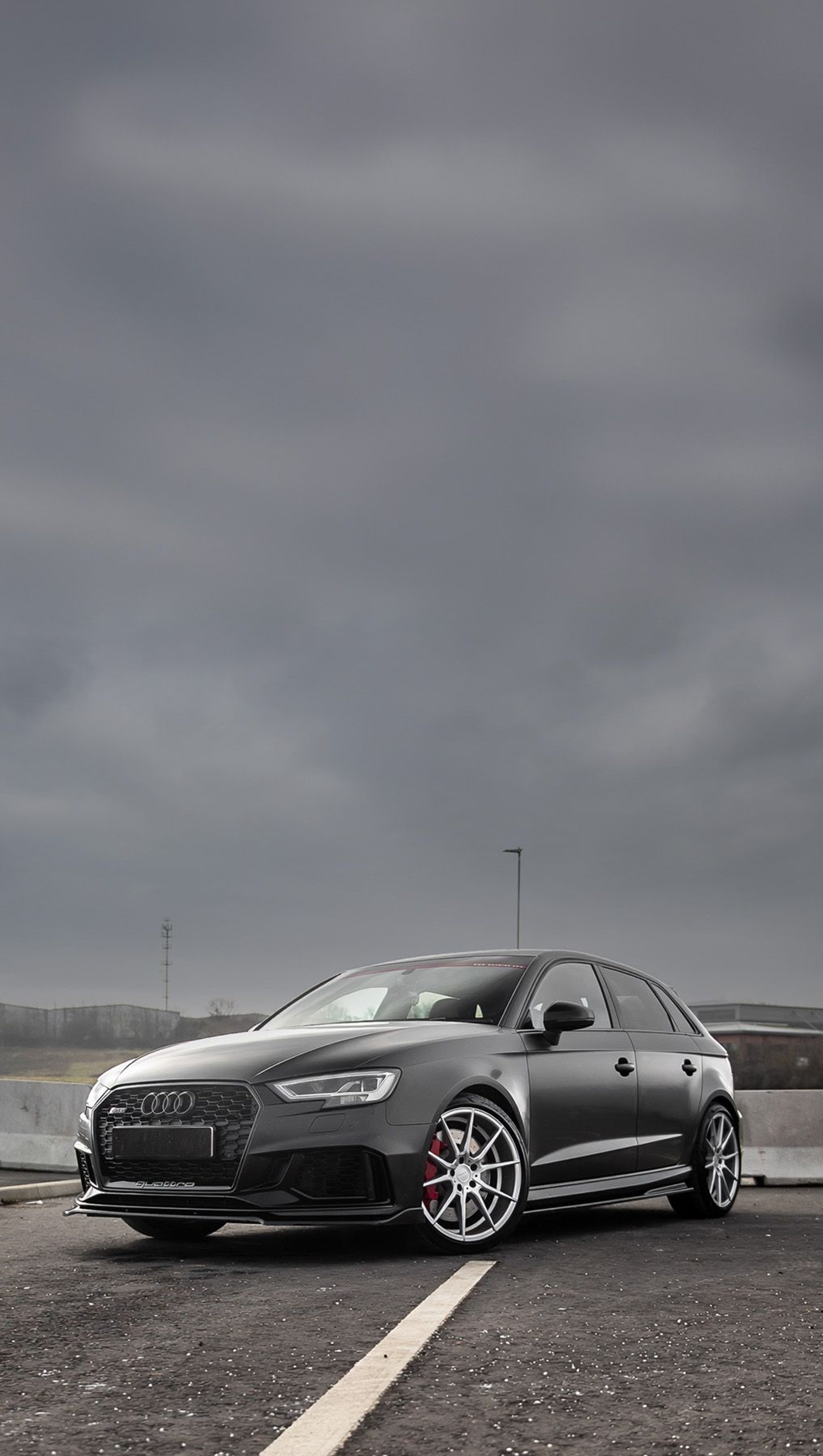 A matte black custom Forge Audi RS3 with silver wheels sits parked on an asphalt lot under an overcast, moody sky.