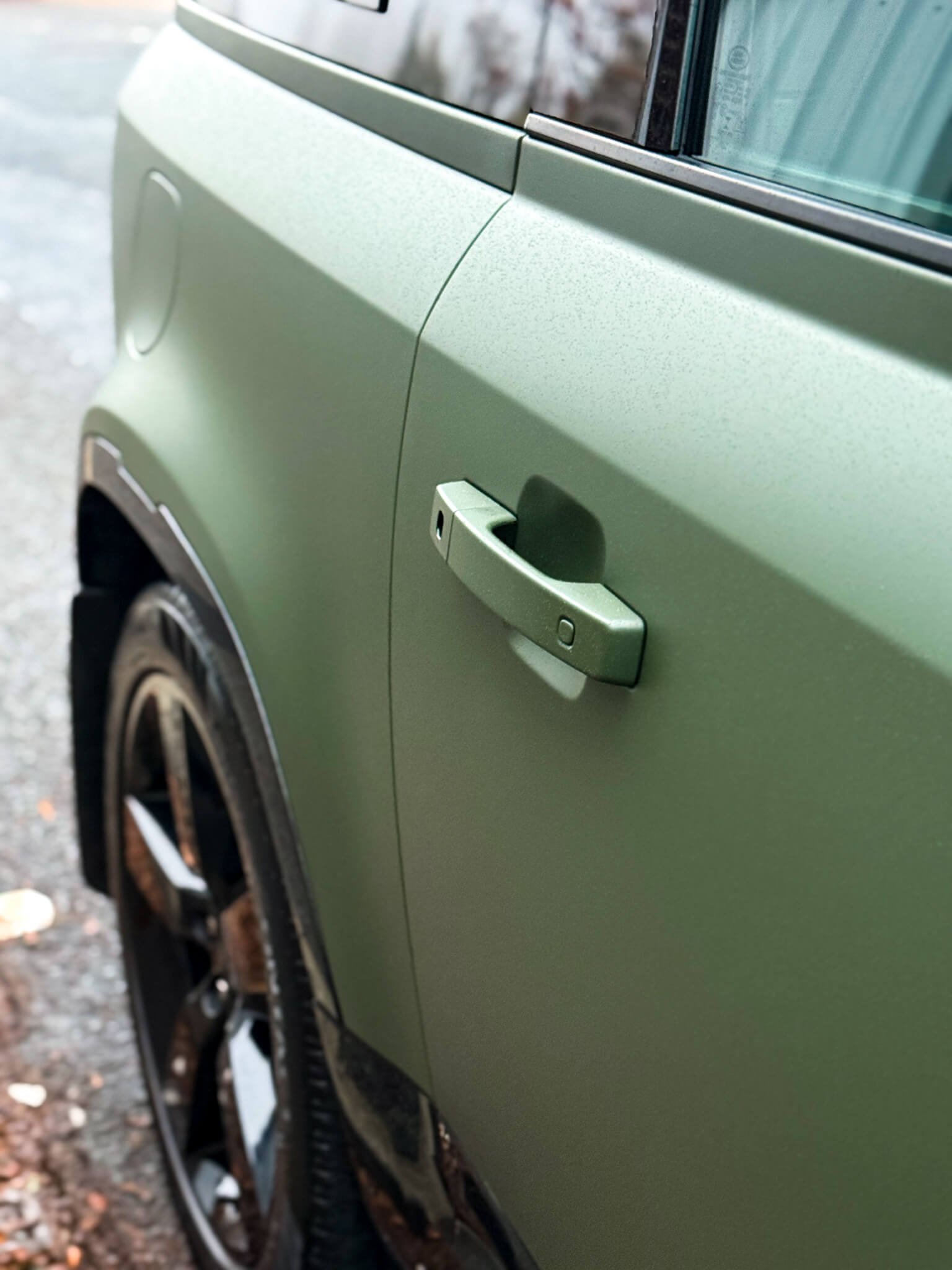 A close-up of a matte green door handle on a custom Forge Land Rover Defender 90 parked outdoors.