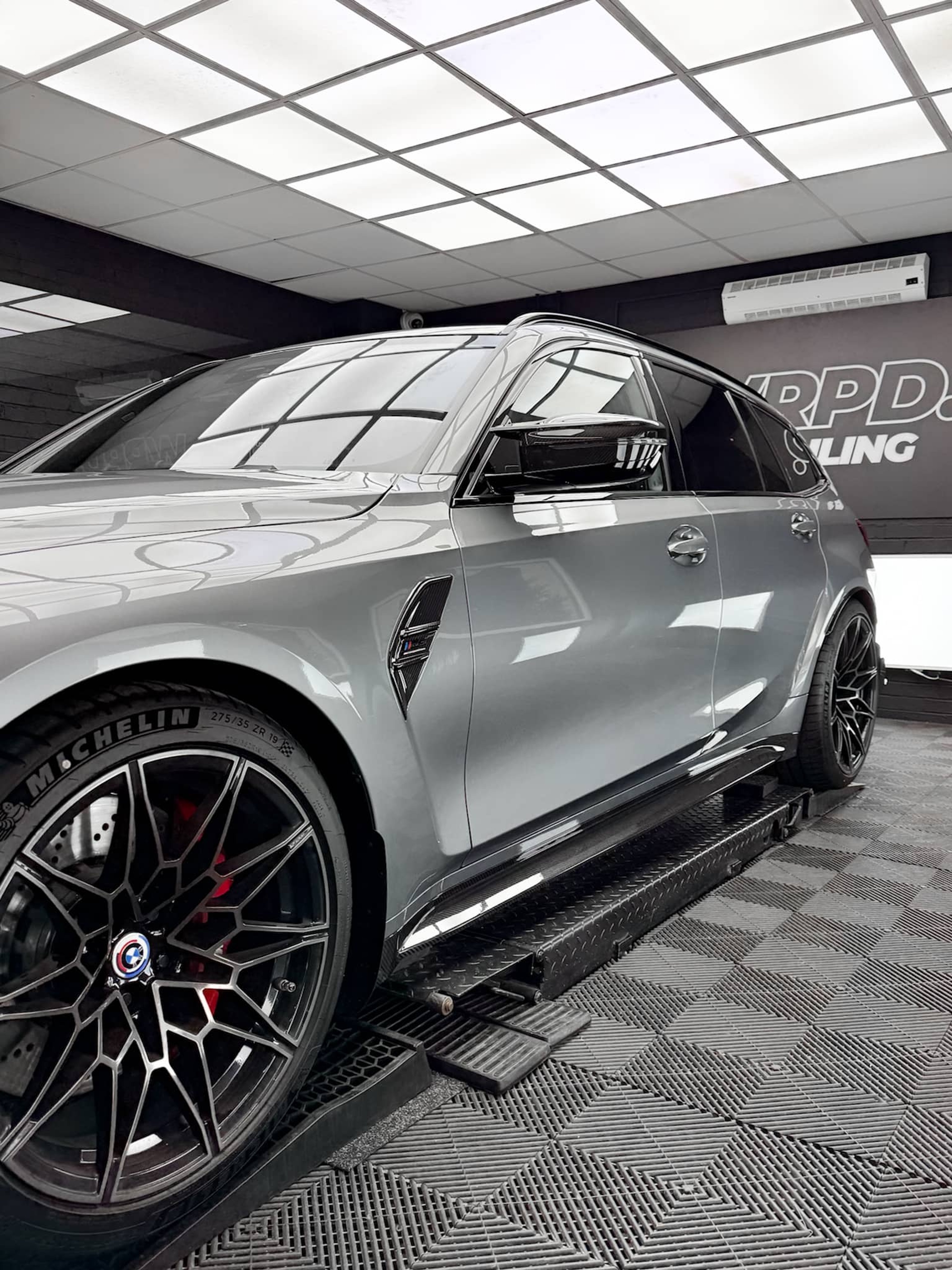 A custom Forge BMW M5 Touring sits elevated on a mechanic lift inside a bright detailing workshop.