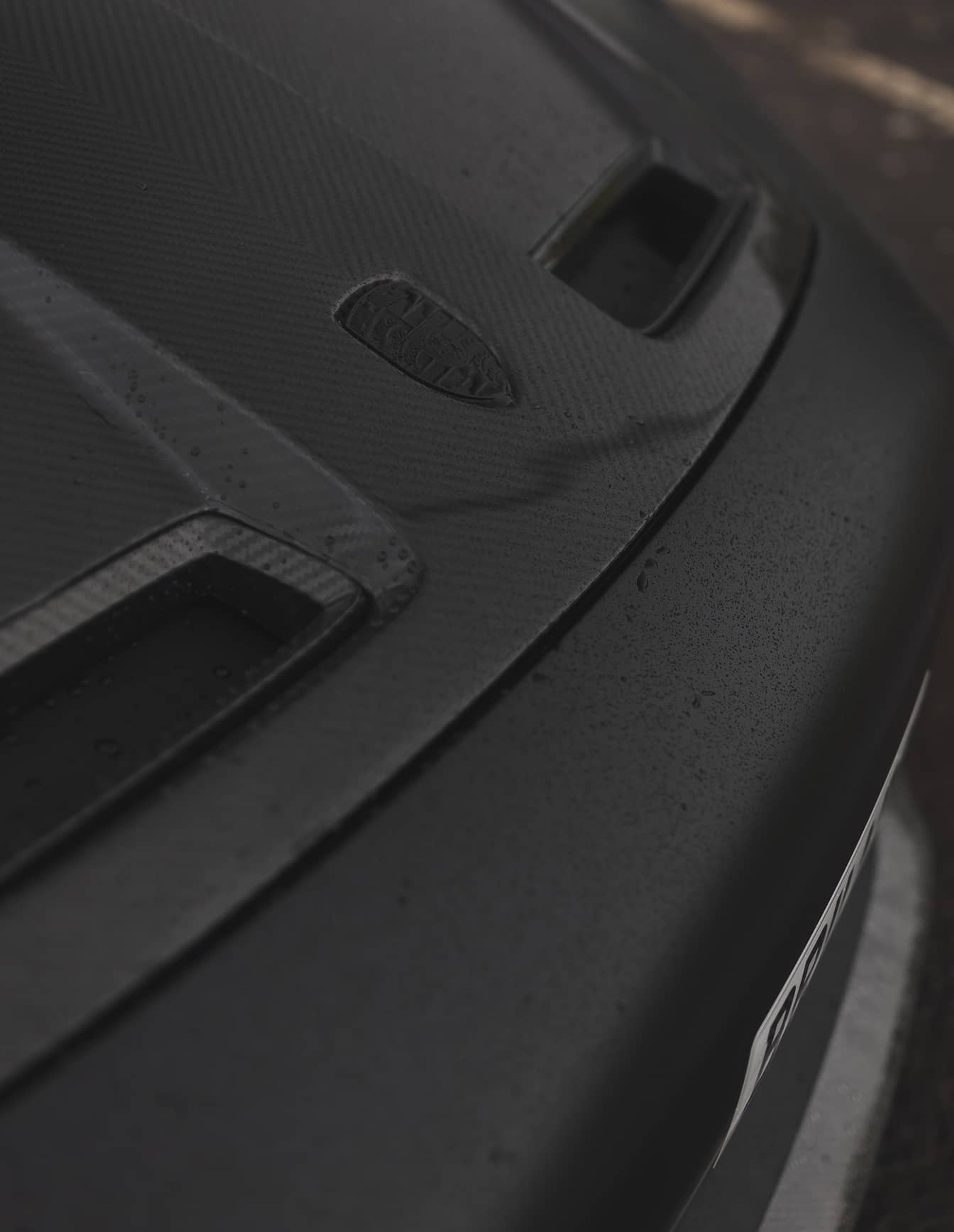 A custom Forge Porsche 911 Carrera Turbo with a carbon fiber hood and vents, lightly covered in raindrops, parked on a wet surface.