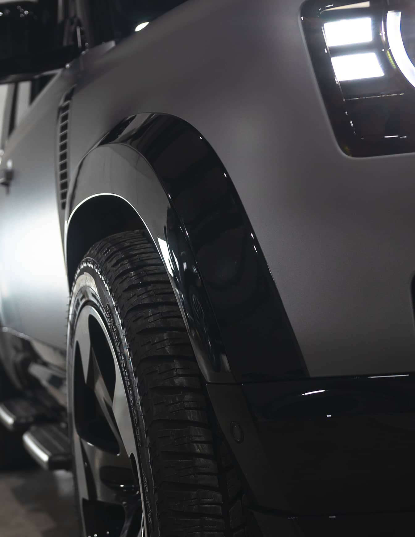 A custom Forge Land Rover Defender 110 with a matte gray finish and glossy black fender flares is parked indoors.