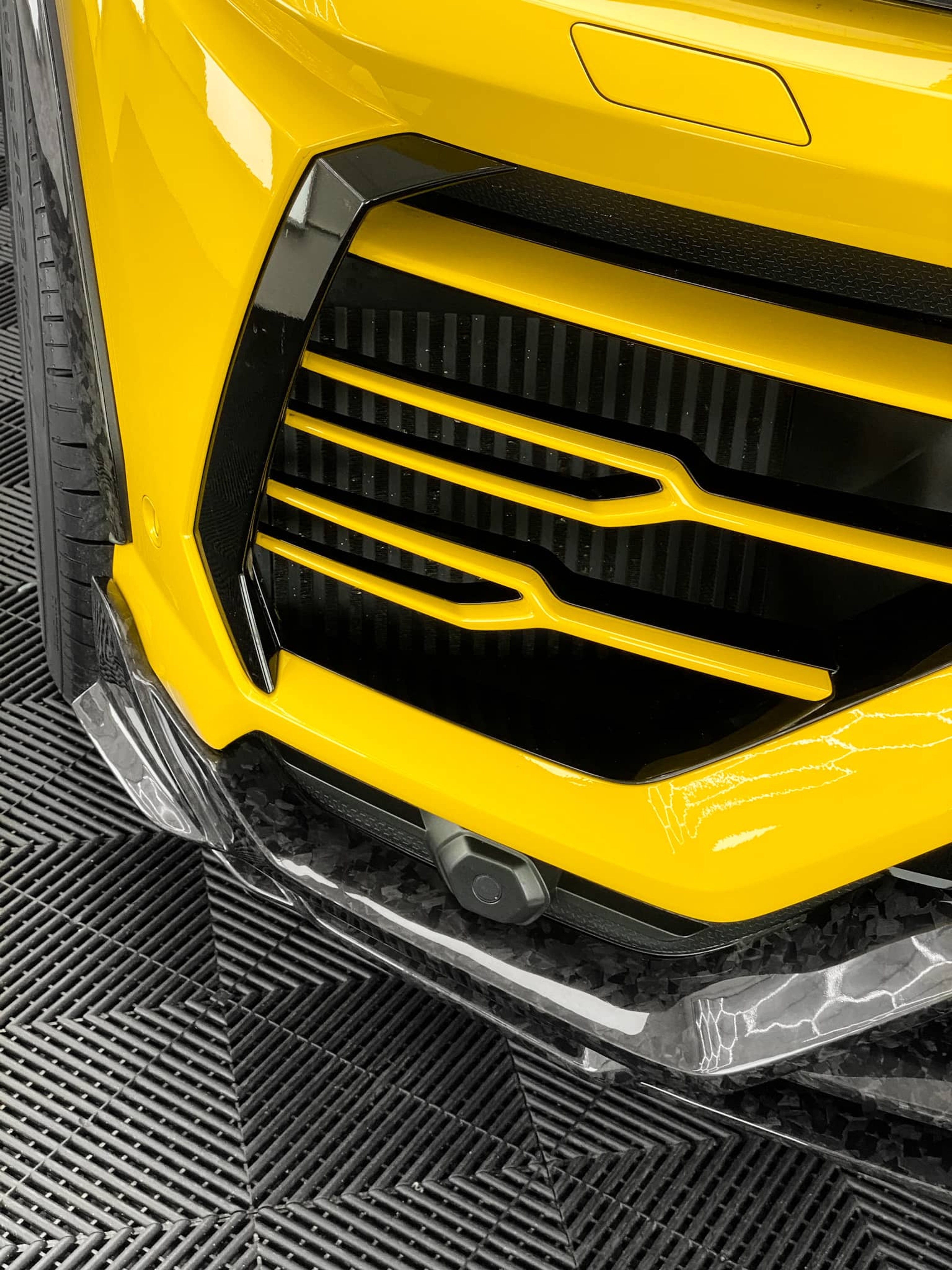 A close-up view shows the yellow front bumper and grille of a custom Forge Lamborghini Urus parked inside a workshop