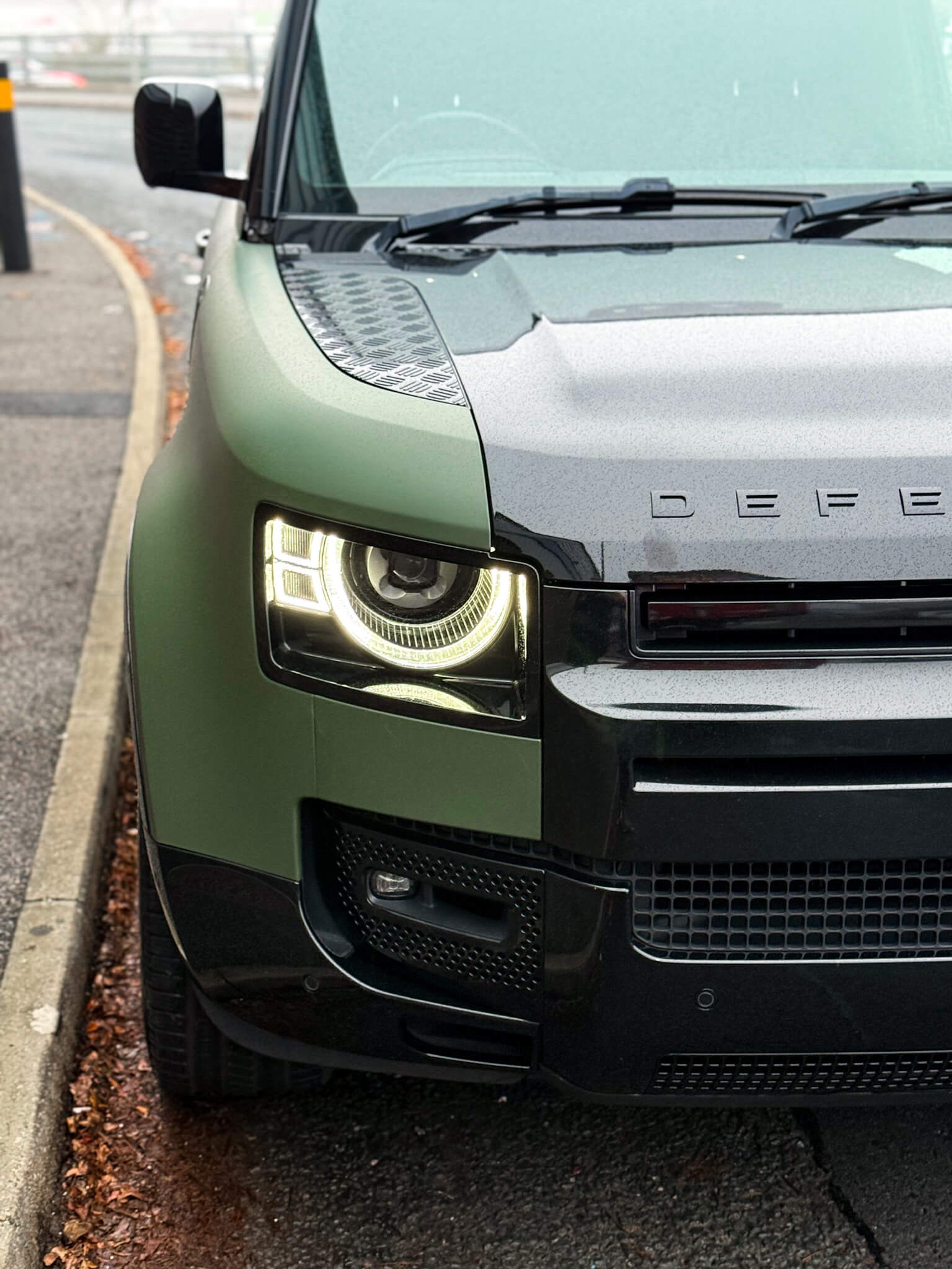 A close-up of a custom Forge Land Rover Defender 90 parked on a roadside with its headlights illuminated.