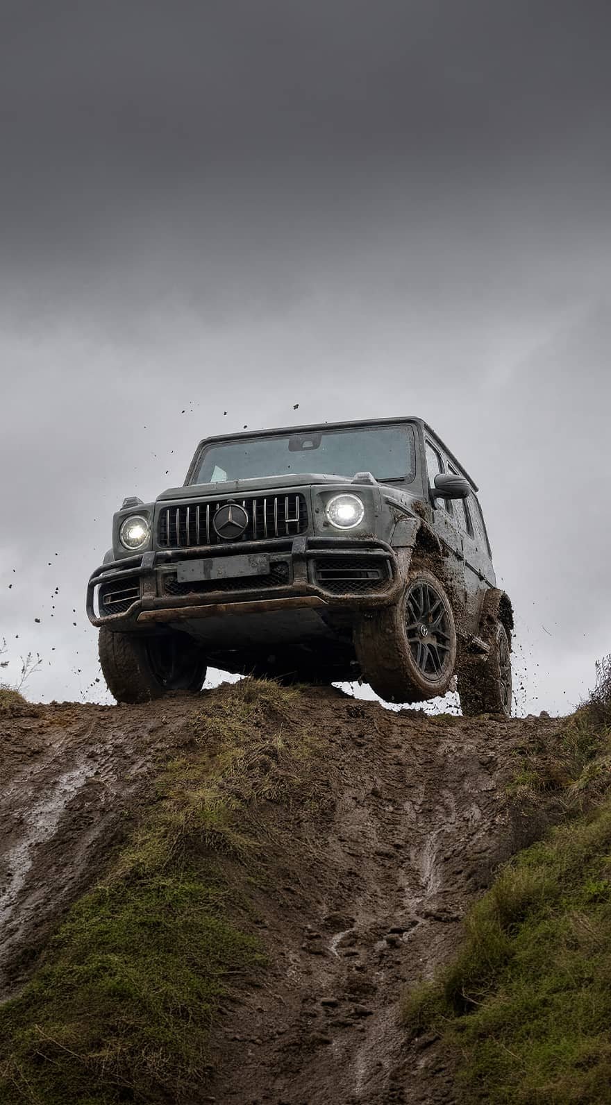 A custom Forge Mercedes G63 navigates a steep, muddy incline beneath an overcast sky.