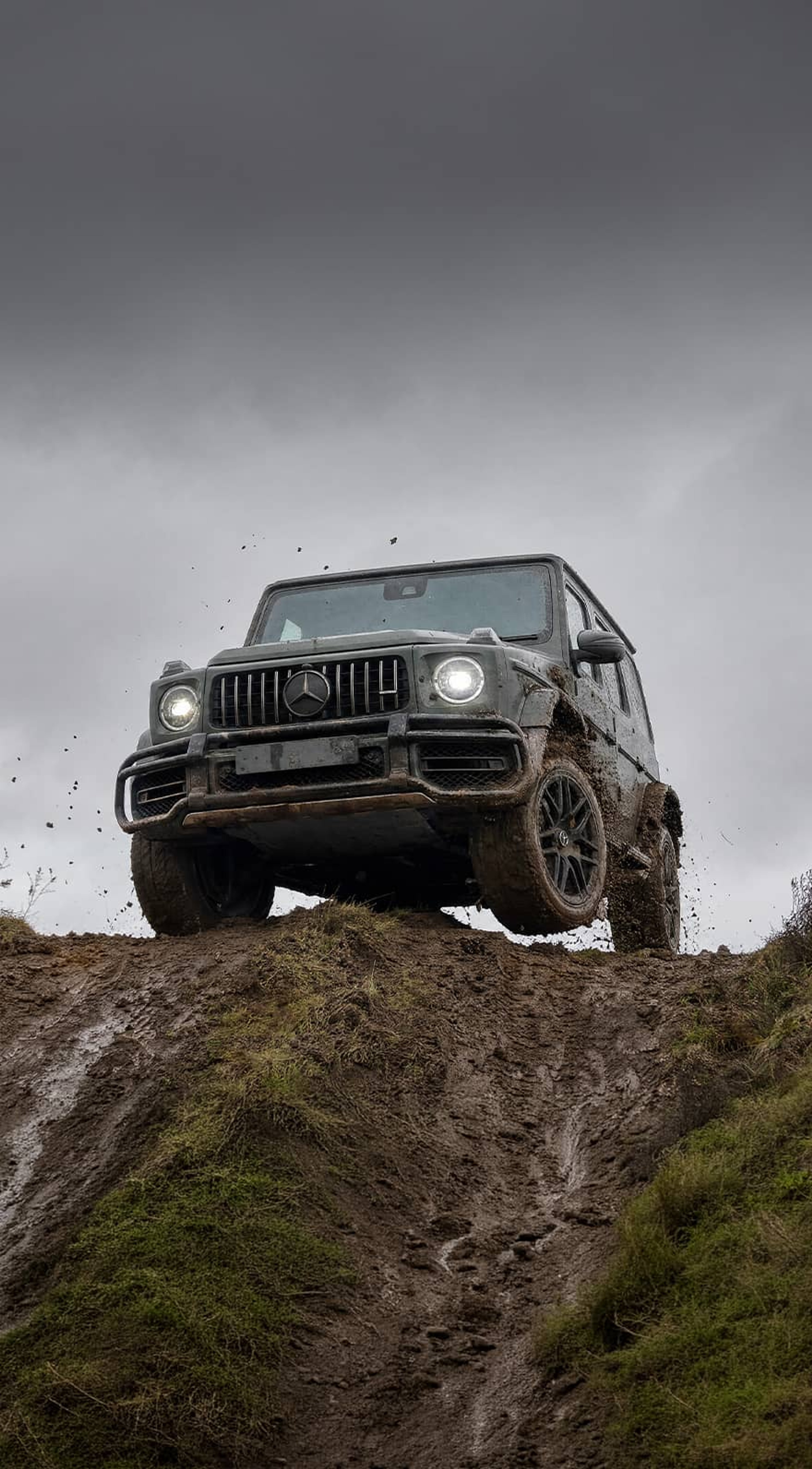 A custom Forge Mercedes G63 navigates a steep, muddy incline beneath an overcast sky.