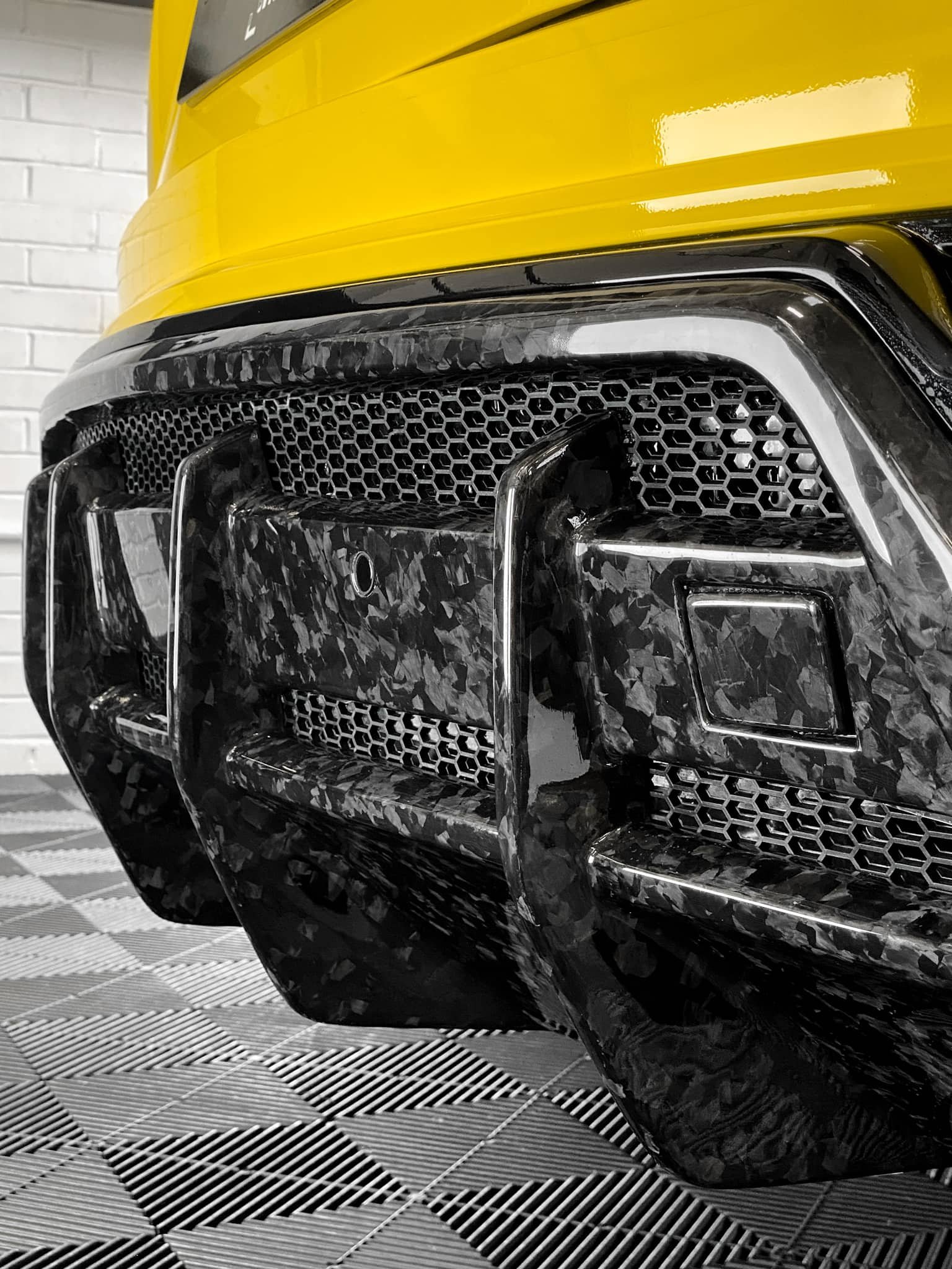 A close-up of the forged carbon fiber rear diffuser on a yellow custom Forge Lamborghini parked on a tiled workshop floor.