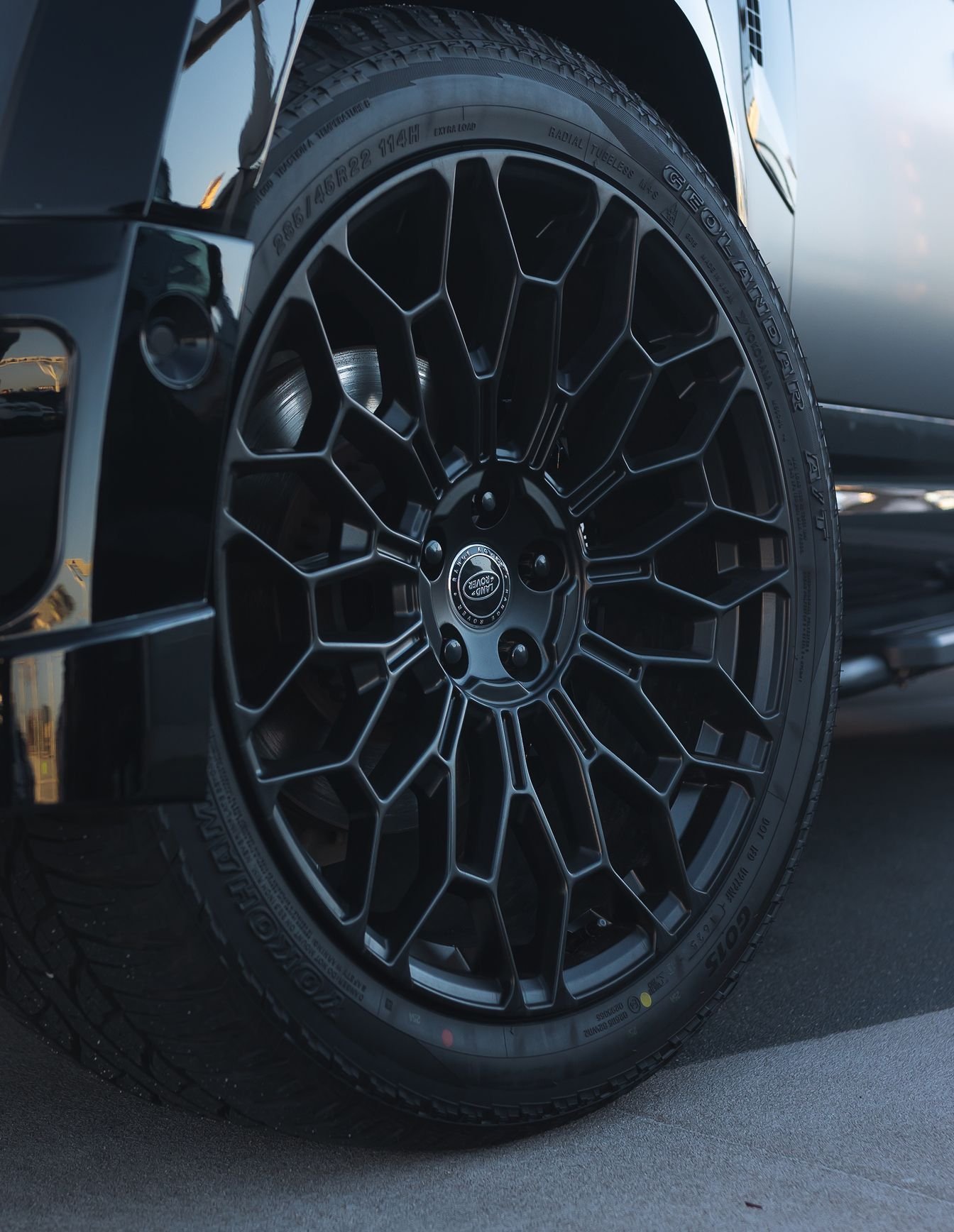 A custom Forge Land Rover Defender 130 wheel with a black geometric spoke design and a Yokohama tire is parked on asphalt.