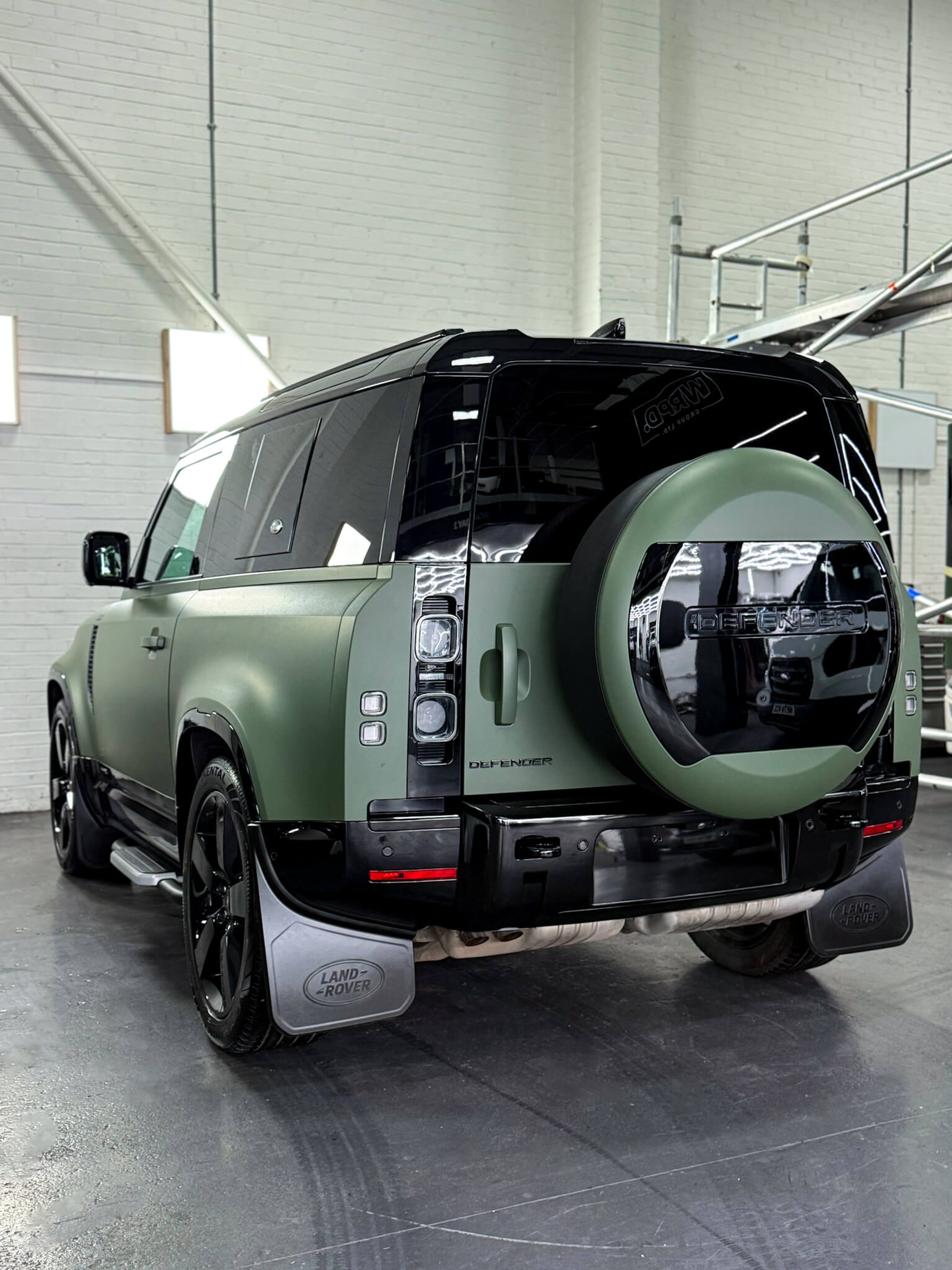 A custom Forge Land Rover Defender 90 with a matte green finish is parked inside a brightly lit workshop.